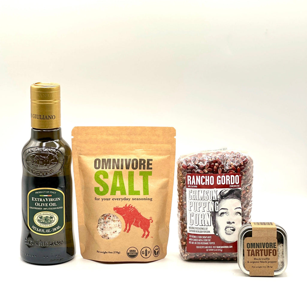 The following products are sitting in a row displayed; 1- 16 oz bag of Rancho Gordo popping corn, 1- 6 oz bag of Omnivore SALT, 1- 2 oz tin of Omnivore Tartufo, and bottle 8.45 FL oz of Extra virgin olive oil