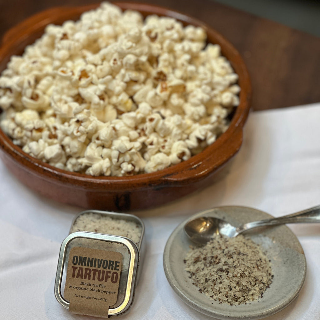 There is a bowl of pop corn with Omnivore 2 oz Tartufo Tin and a salt dish with Tartufo in it with a small silver spoon