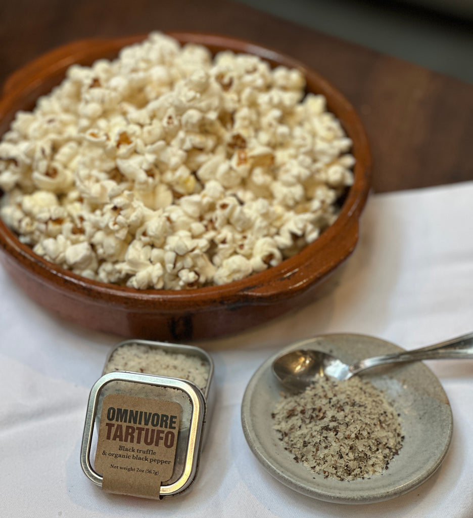 There is a bowl of pop corn with Omnivore 2 oz Tartufo Tin and a salt dish with Tartufo in it with a small silver spoon