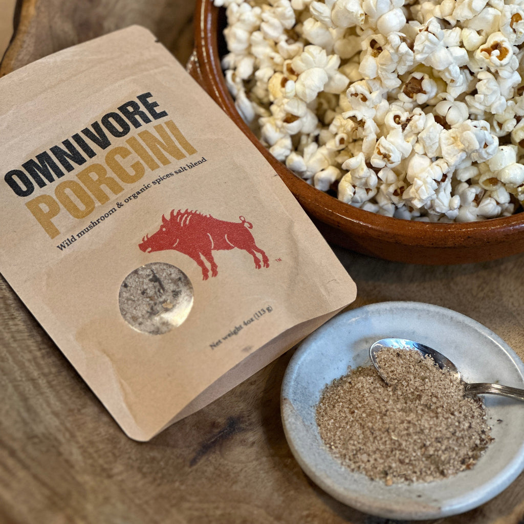 a bowl of popcorn with a 6 oz bag of Omnivore Porcini salt and a salt dish with a spoon and some porcini salt